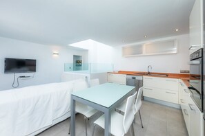 A modern kitchen with a dining area, a TV mounted on the wall, and a window providing natural light.