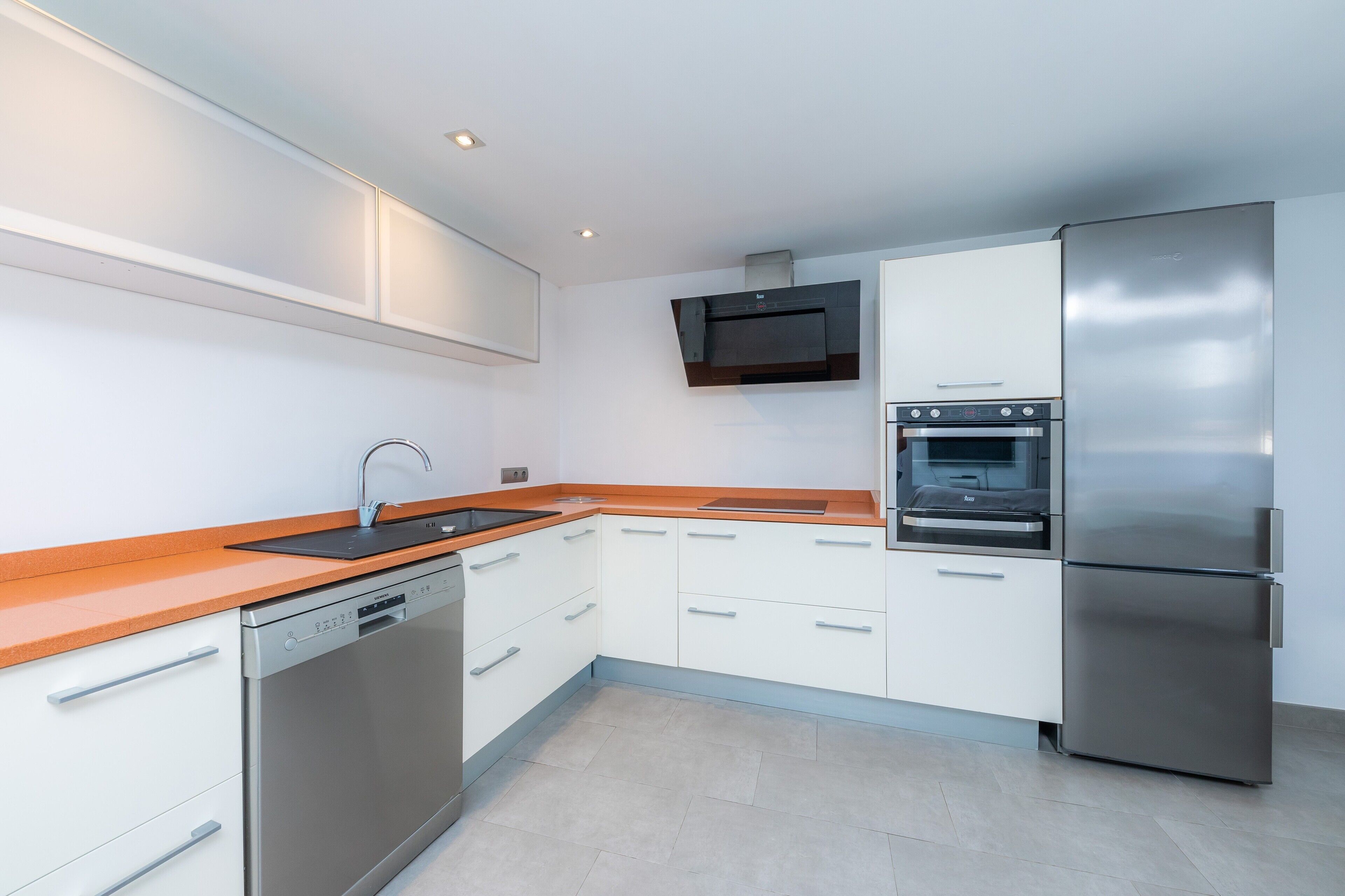 A modern kitchen with white cabinets, stainless steel appliances, and a wooden countertop.