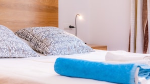 Een opgemaakt bed met gestreepte kussens, een houten hoofdbord, een nachtkastje met een lamp en een raam met gordijnen.