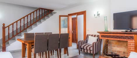Un salon avec un escalier en bois, un coin repas avec des chaises, un canapé, une cheminée et un téléviseur.