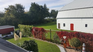 A white building with a metal roof, surrounded by a well-maintained garden with red foliage and a lawn. - Apartment lake view (Glücksburg (Ostsee))