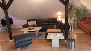 A cozy living room with a black leather sofa, two coffee tables, a blue ottoman, and a potted plant. - Apartment lake view (Glücksburg (Ostsee))