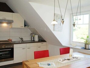 Een moderne keuken met witte kasten, een ingebouwde oven en rode stoelen. Een raam zorgt voor daglicht en uitzicht op groen.