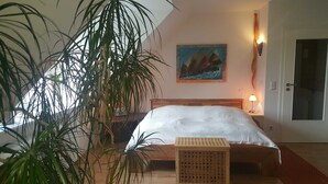 A bedroom with a bed, a nightstand, a lamp, a painting, and a door. - Apartment lake view (Glücksburg (Ostsee))
