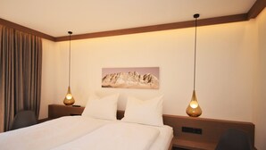 A hotel room with a large bed, two bedside tables, a desk, a chair, and a painting on the wall.