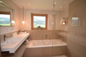 Ein modernes Badezimmer mit einer großen Badewanne, zwei Waschbecken und einem Fenster mit Blick auf die Landschaft.