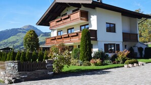 A two-story chalet with wooden balconies, a stone facade, and a mountain backdrop.
