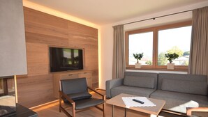 A modern living room with a grey sofa, a wooden coffee table, a black chair, and a TV mounted on the wall.