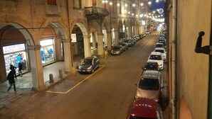 Eine Straße mit parkenden Autos und Gebäuden mit Rundbogenfenstern, links ein Geschäft.