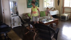 A living room with a sofa, chairs, a coffee table, a television, and a ceiling fan. - Makaha on the Beach-Back in Time =Direct Oceanfront & Cove (Waianae)