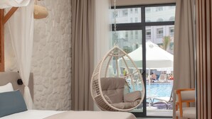 A bedroom with a bed, a hanging chair, a view of a pool, and a window with curtains. - Side Royal Style Hotel (Manavgat)