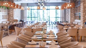 A spacious dining area with long tables, comfortable chairs, hanging pendant lights, and greenery. - Side Royal Style Hotel (Manavgat)