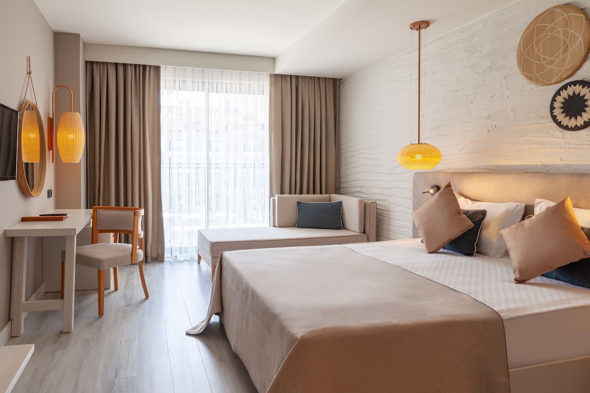 Habitación de hotel con cama, escritorio, silla y sofá. Hay dos lámparas colgantes y un televisor en la pared.
