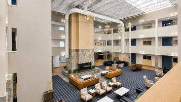 A spacious lobby with a stone fireplace, multiple seating areas, and a high ceiling with visible structural beams.