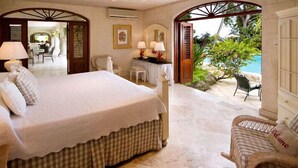 Un dormitorio con una cama grande, un escritorio con dos lámparas y vistas a un espacio exterior con piscina y vegetación.