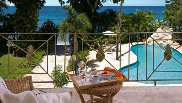 Zona junto a la piscina con vista al océano, una silla de mimbre, una mesa con una bandeja de comida y una tumbona.