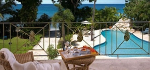 Zona junto a la piscina con vista al océano, una silla de mimbre, una mesa con una bandeja de comida y una tumbona.