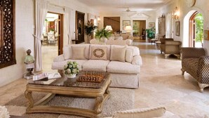 Un salón amplio con un sofá color beige, una mesa de centro de madera y un sillón estampado.