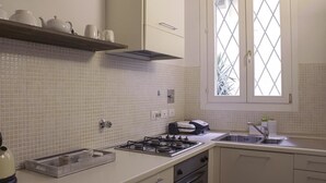 Eine Küche mit weiß gefliestem Rückspritzschutz, einem Gasherd, einem Spülbecken und einem Fenster mit Blick auf Grünflächen.