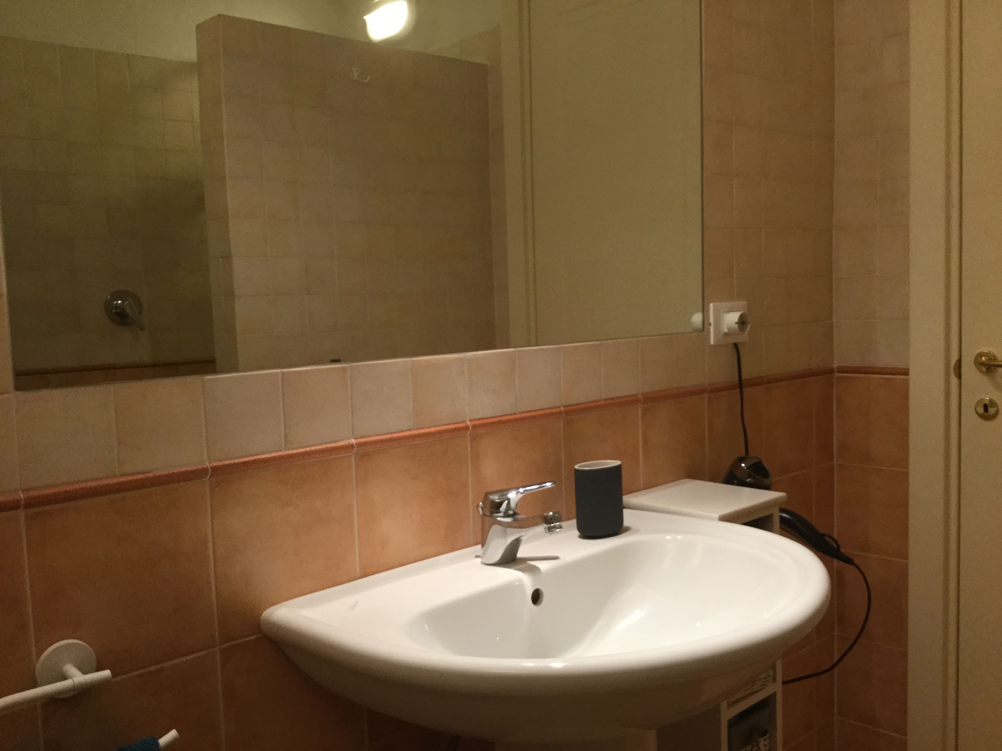 Egy fürdőszoba, amelyben fehér mosdókagyló, tükör és törölközőtartó található.