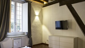 Ein Schlafzimmer mit Bett, Wandfernseher, Heizkörper und einem Fenster mit Vorhängen.