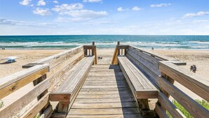 Une promenade en bois qui mène à une plage offrant une vue dégagée sur l’océan.