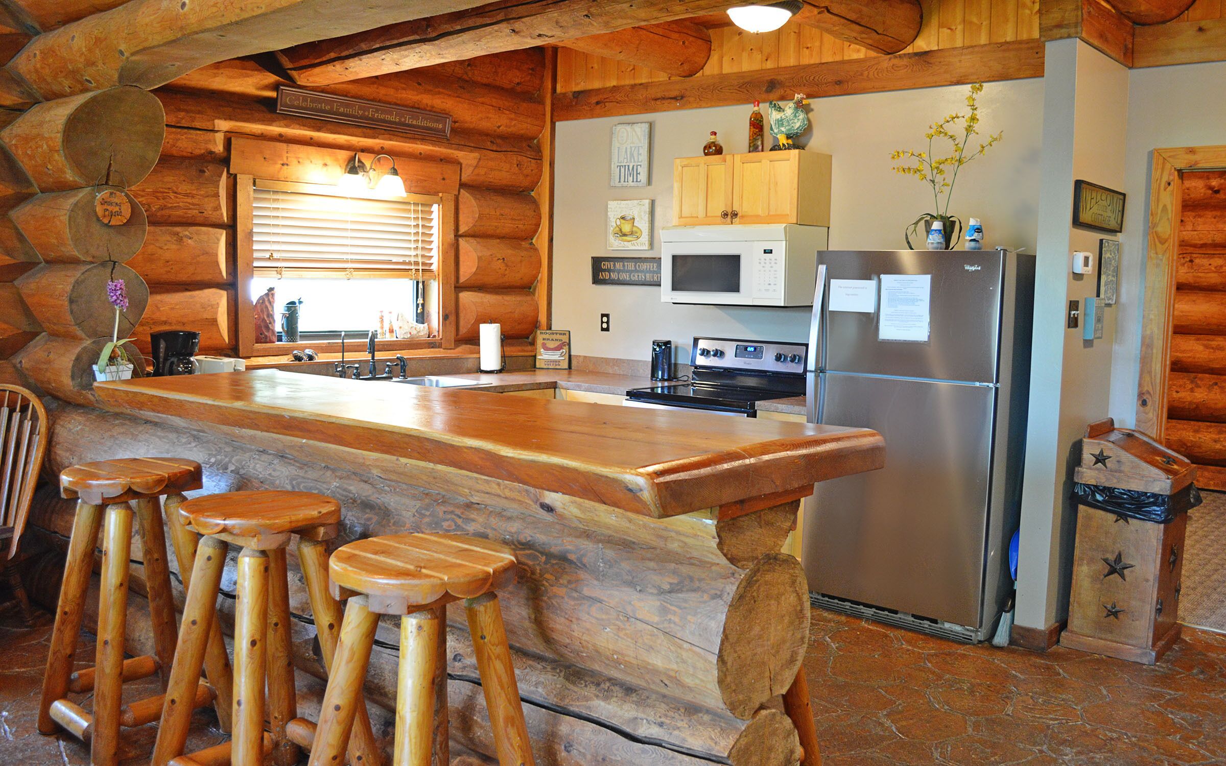 A rustic kitchen with wooden bar stools, a stainless steel refrigerator, and a wooden countertop.