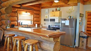 A rustic kitchen with wooden bar stools, a stainless steel refrigerator, and a wooden countertop. - Lakefront Cabin w/ Loft • Sleeps 12 • Amenities (Burnet)