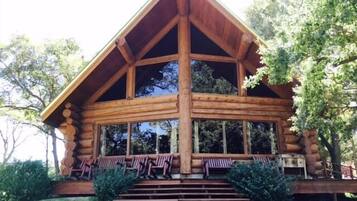 A log cabin with a large porch, multiple windows, and a staircase leading to the entrance.