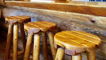 A wooden bar area with three stools, a wooden counter, and a kitchen area with a microwave and cabinets.