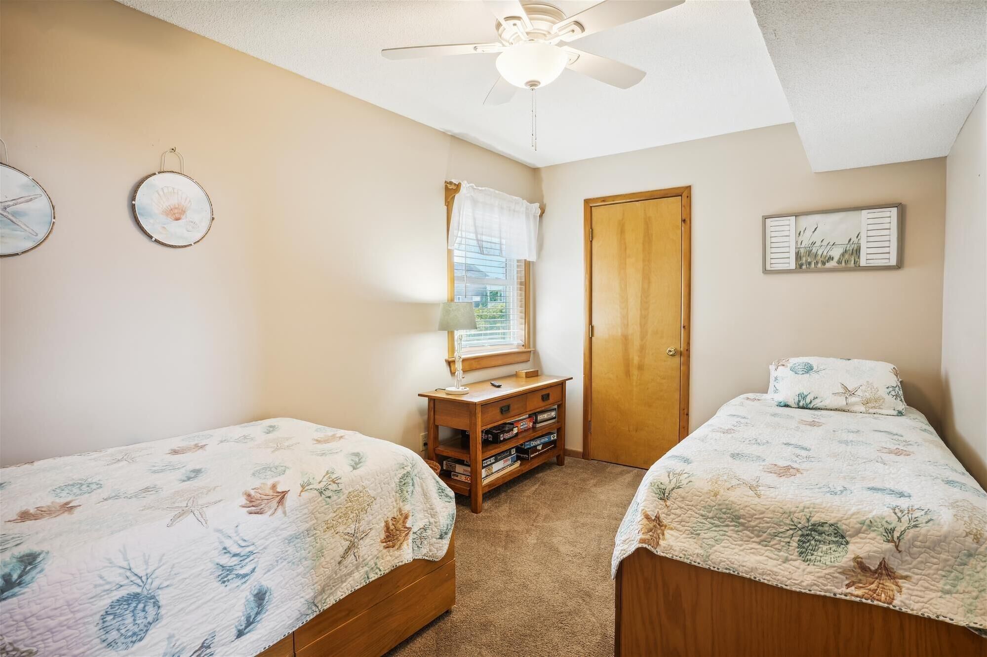 A bedroom with two beds, a wooden dresser, a ceiling fan, and a window with blinds.