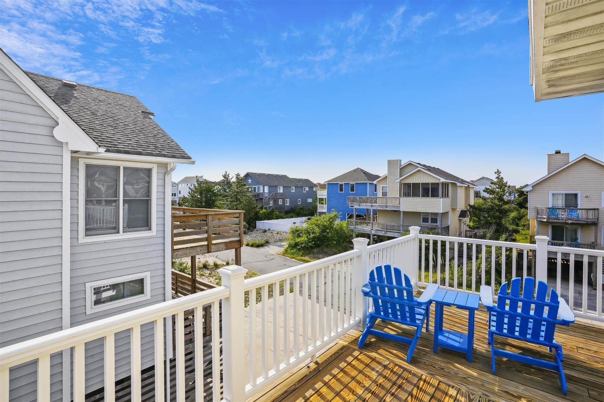 Une terrasse avec des fauteuils Adirondack bleus et une petite table, donnant sur un quartier résidentiel avec des maisons.