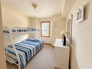 A bedroom with bunk beds, a desk, a lamp, and a window.