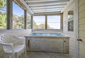 A hot tub in a covered outdoor area with a wooden deck, a white plastic chair, and large windows. - Private pool, Hot Tub! (Corolla)