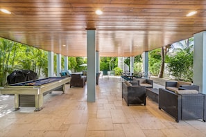 Relax in a tranquil outdoor space with a pool table and comfortable seating, surrounded by lush greenery.