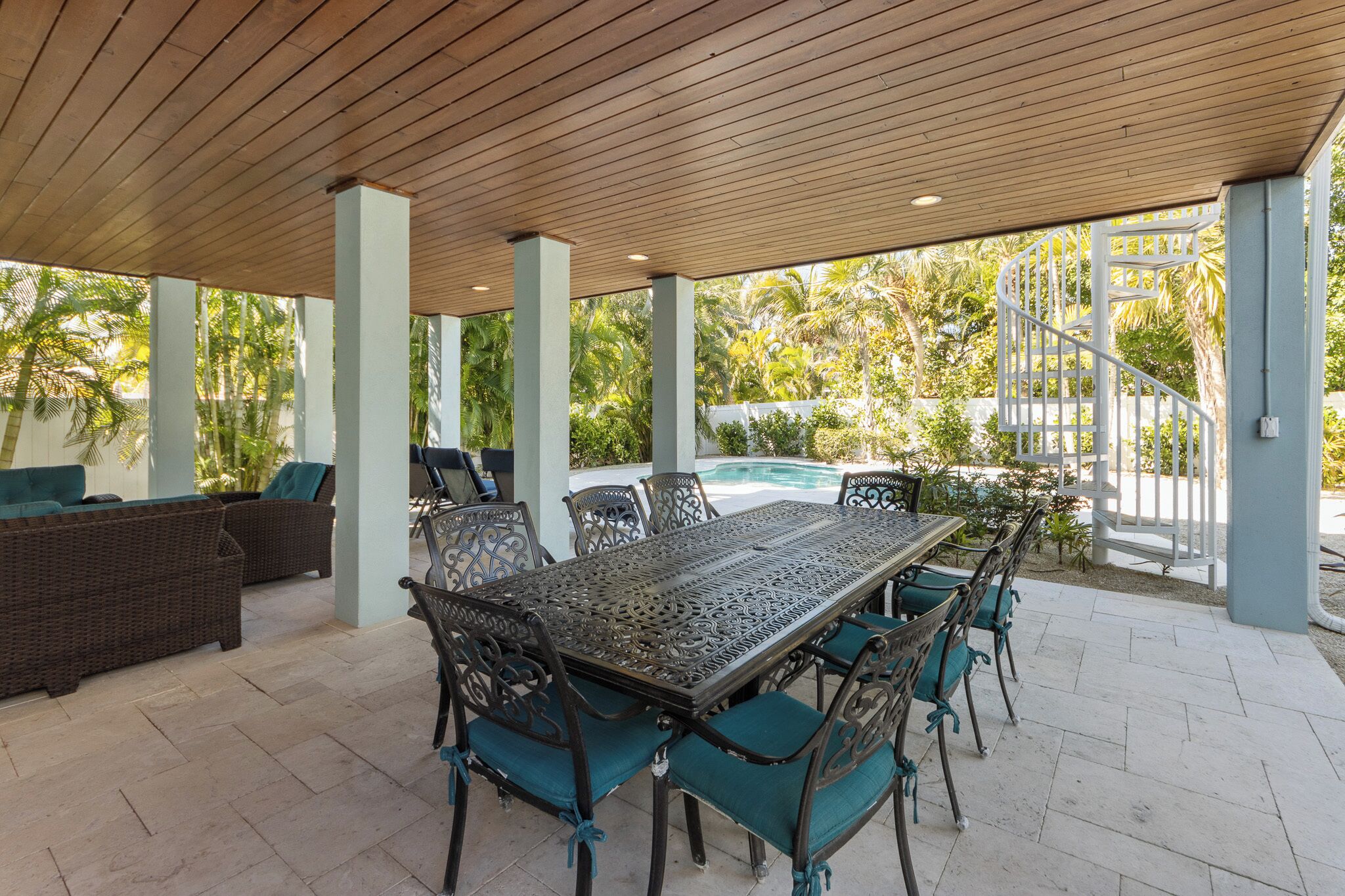 An outdoor patio with a pool, covered seating, and a spiral staircase.