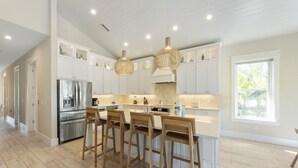 A modern kitchen with white cabinetry, a stainless steel refrigerator, wooden bar stools, and pendant lighting. - 4 Beds 4.5 Bath with Pool 3 Blocks to Beach (Anna Maria)
