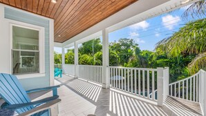 A covered porch with white railings, a blue Adirondack chair, and a view of lush greenery. - 4 Beds 4.5 Bath with Pool 3 Blocks to Beach (Anna Maria)