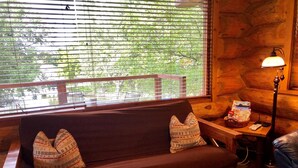 A wooden cabin interior with a sofa, pillows, a lamp, and a table with magazines.