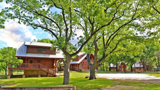 A rustic log cabin with a porch and a staircase leading to a deck.