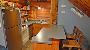 A compact kitchen with wooden cabinets, a granite countertop, a refrigerator, a sink, and a bench with chairs.