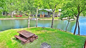 A lakeside patio with a wooden picnic table and a fire pit.