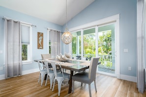 A dining area with a wooden table, white chairs, and a hanging light fixture.