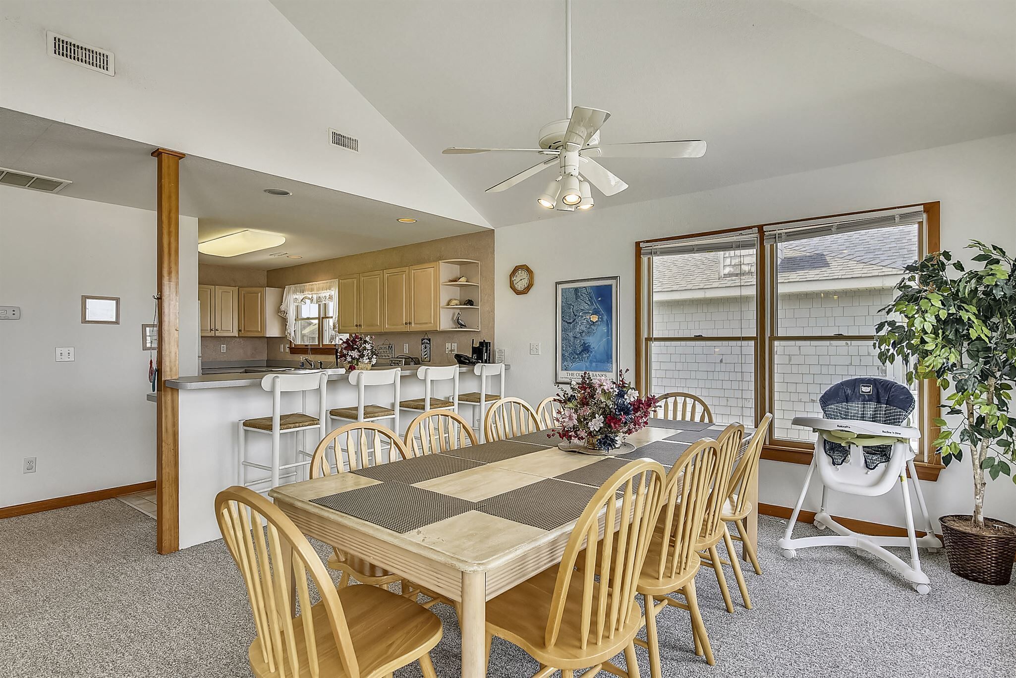 A dining area with a large wooden table, chairs, a ceiling fan, and a view of the kitchen.