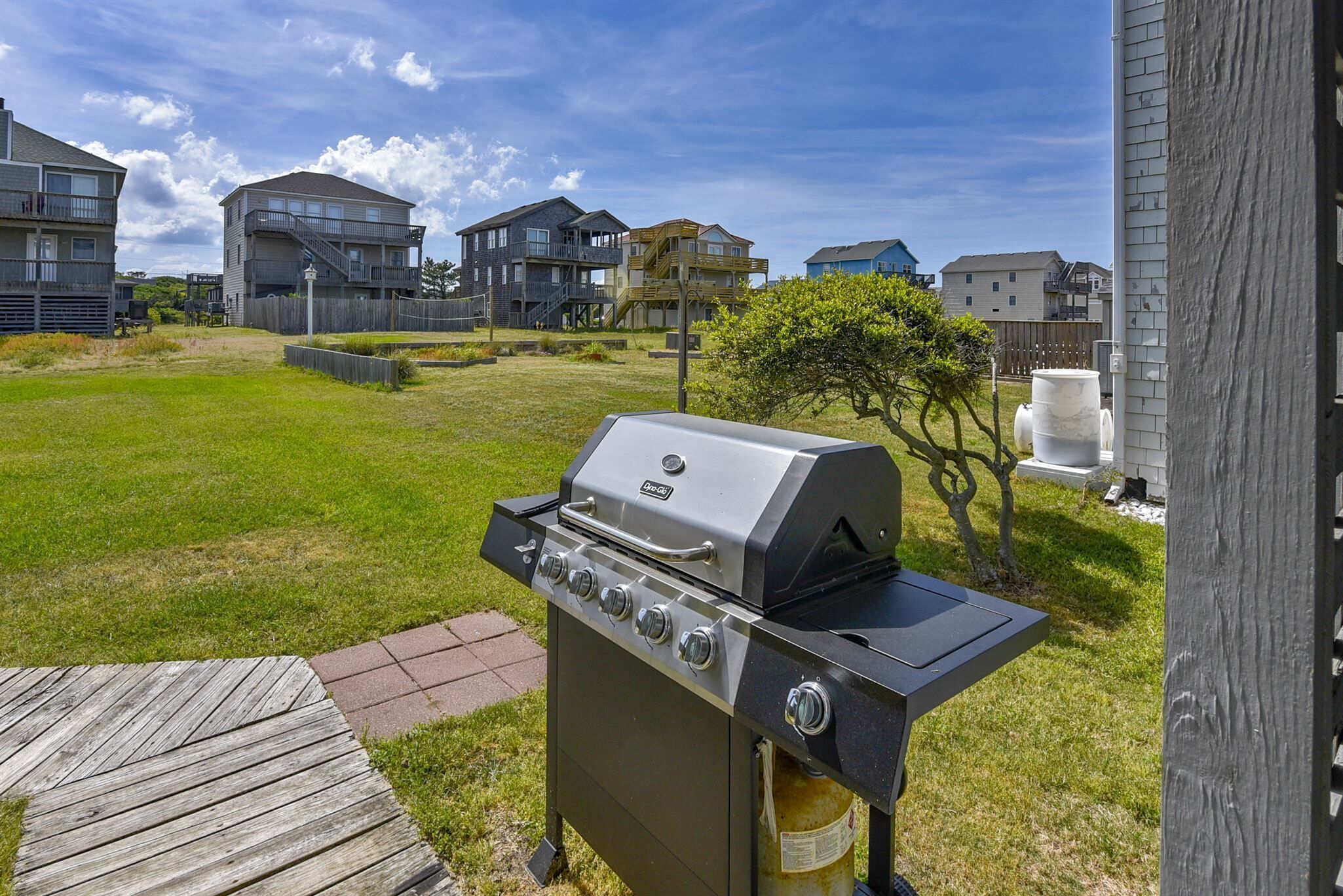 Un jardin avec un barbecue intégré, une terrasse en bois et une pelouse verdoyante.