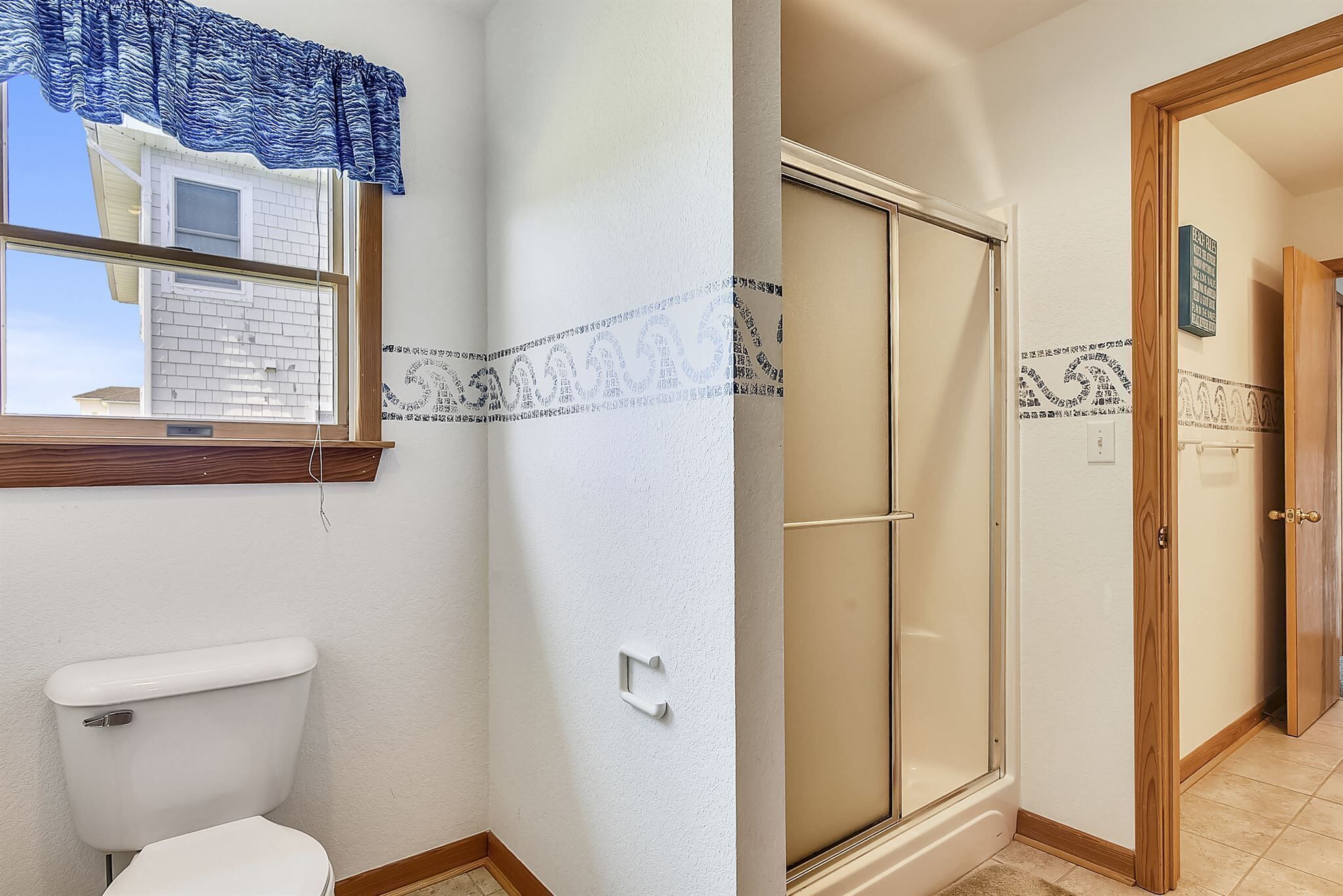 Ein Badezimmer mit Toilette, einem Fenster mit blauem Vorhang und einem Duschbereich mit Glastür.
