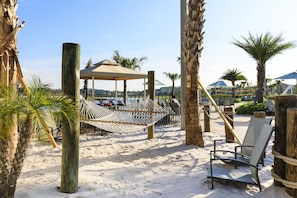 Relax in a serene beach setting with a hammock and lounge chair, surrounded by palm trees and a gazebo.