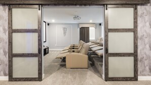 A home theater room with a large screen, multiple seating areas, and a carpeted floor. - Modern Luxury Villa with Everything (Kissimmee)