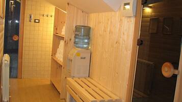 Una sauna con pareti in legno, una panca, un distributore di acqua e un portascopevoli.