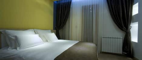 A hotel room with a bed, curtains, a window, and a radiator.
